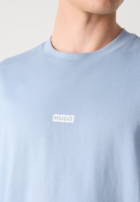 Ljusblå t-shirt med kort ärm, tillverkad av mjuk bomull, med en vit "HUGO"-logotyp på bröstet och en klassisk rund halsringning.