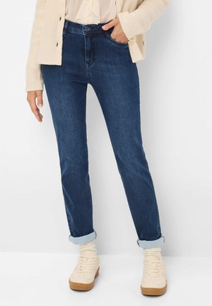 Jeans in jeans scuro con un design aderente, caratterizzati da risvolti sulle caviglie, passanti per la cintura e tasche frontali. Abbinati a sneaker alte beige.