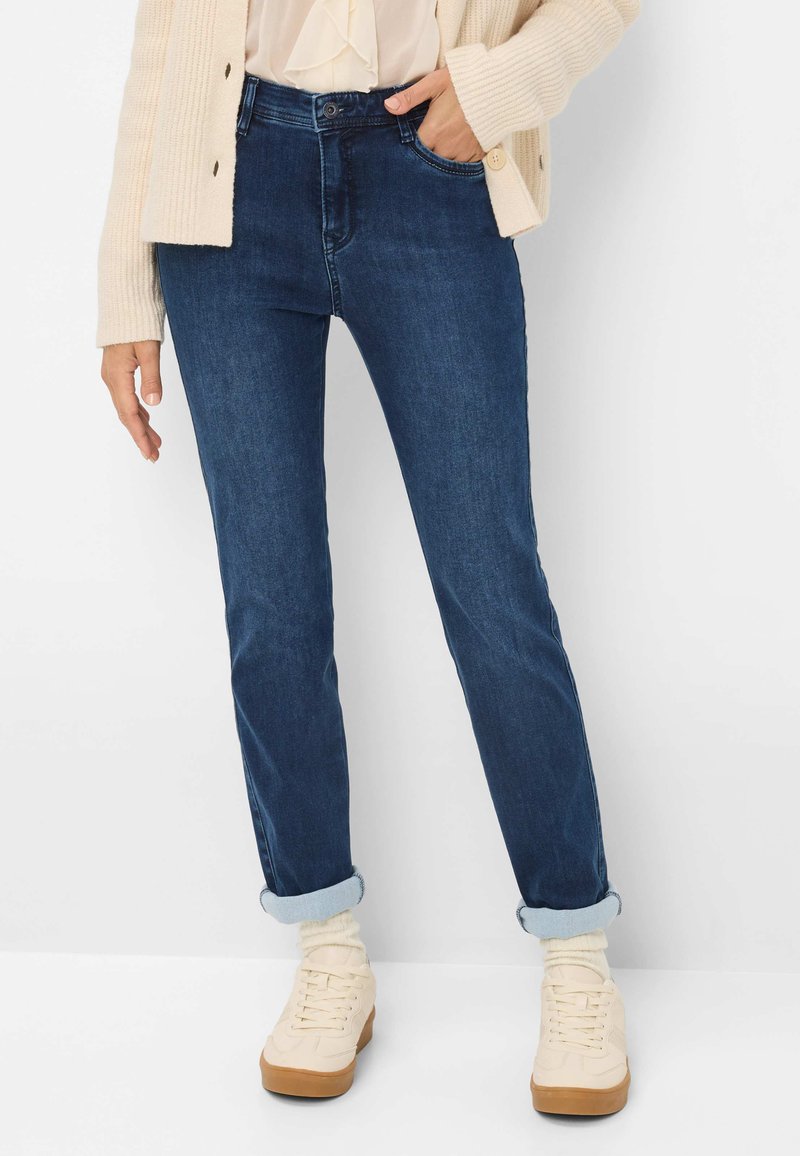 Jeans en denim bleu foncé au design ajusté, avec des ourlets retroussés, des passants de ceinture et des poches avant. Associés à des baskets montantes beiges.