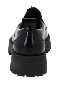 Chaussure en cuir verni noir avec semelle à crampons épaisse, languette de talon visible et couture apparente à l'arrière, vue de dos.