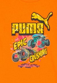 Helles oranges Hintergrund mit einem rissigen PUMA-Logo, zwei bunten Monstertrucks, die rote Autos zerquetschen, und dem fetten Text "Epicke Zerschlagung."