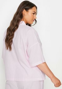 Vaaleanpunainen lyhythihainen paita, jossa on valkoisia pystysuoria raitoja, rento malli ja litteä kaulus. Pehmeä tekstuuri, takanäkymässä on minimaalista yksityiskohtaa.