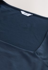 Blusa di cotone blu navy con una texture liscia, caratterizzata da un ampio scollo e dall'etichetta del marchio visibile sul retro.