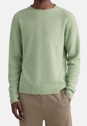 Pull en maille vert clair avec un col rond, des poignets et un ourlet côtelés, coupe oversize, associé à un pantalon à motif pied-de-poule.