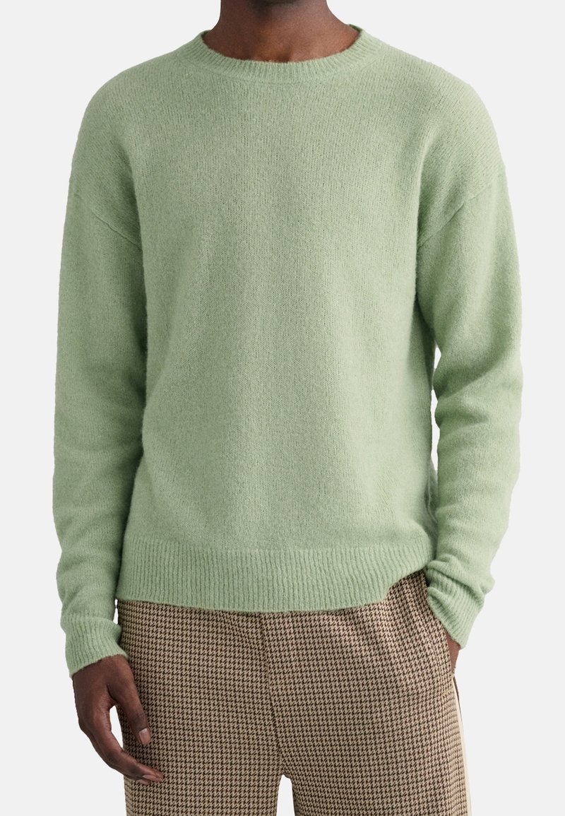Maglione a maglia verde chiaro con scollo rotondo, polsi e orlo a coste, vestibilità oversize, abbinato a pantaloni con motivo a scapito di cane.