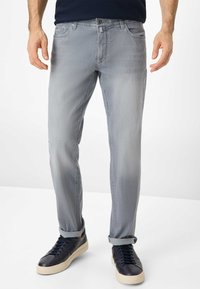 Hellgraue Jeans im Slim-Fit, mit fünf Taschen, Gürtelschlaufen und umgeschlagenen Säumen. Kombiniert mit dunkelblauen Sneakers. Glatte Denim-Textur.