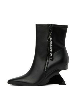 Bottine en cuir noir avec bout pointu, talon sculpté courbé, fermeture éclair latérale et tirette portant l'inscription "Choose me or you lose me."