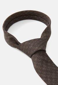 Cravate marron à texture avec une finition lisse, présentant un design en boucle et un motif subtilement tacheté. Le tissu semble doux et flexible.