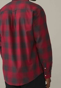 Camisa de cuadros en rojo y negro de manga larga, con cuello abotonado, pliegue en la espalda y puños con un solo botón. Fabricada en un tejido suave y texturizado.