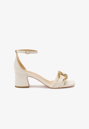 Sandalo bianco con tacco, dotato di cinturino alla caviglia, tomaia testurizzata con una fibbia accentuata in oro e un tacco quadrato. Design semplice e minimalista.