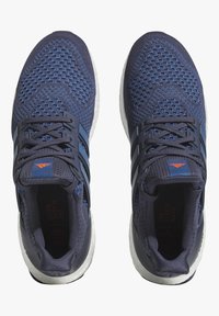 Sapatilhas atléticas azul marinho com parte superior em malha texturizada, três riscas escuras e uma entressola branca apresentando a inscrição "Acabar com o Lixo Plástico" na palmilha.