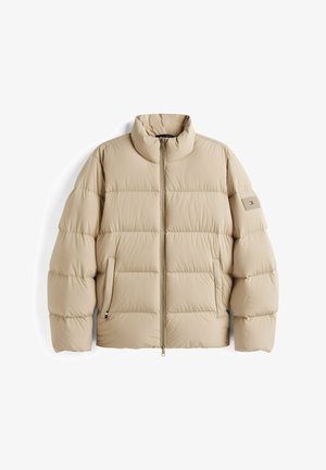 Beige pufferjack met een hoge kraag, doorgestikt ontwerp, zijzakken en een merkembleem op de linkermouw. Met ritssluiting aan de voorkant.