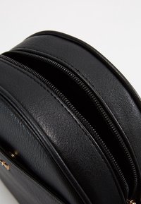 Černá kožená taška s dvěma zipovými oddíly, zaobleným tvarem, texturovaným povrchem a zlatými kovovými doplňky.