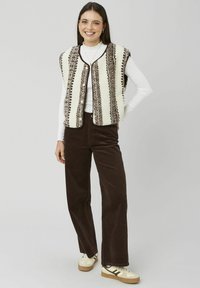 Gilet en polaire crème avec motifs géométriques marron, fermeture à boutons et encolure arrondie. Associé à un pantalon en velours côtelé marron et des baskets.