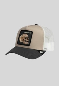 Casquette trucker en mesh beige et blanche avec une visière gris foncé, ornée d'un patch représentant un crâne marron et le mot "CANCELLED" sur le panneau avant.