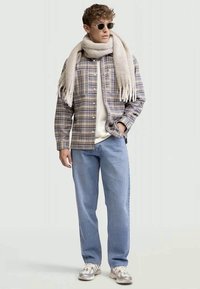 Camisa xadrez em cores suaves, cachecol creme, t-shirt branca, jeans azul claro e ténis cinzentos. Os acessórios incluem óculos de sol redondos.