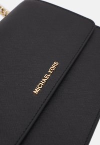 Zwarte leren portemonnee met een gouden "MICHAEL KORS" logo-accent. Heeft een slanke vorm en een schoon, modern ontwerp.