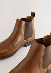Braune Chelsea-Stiefel aus Leder mit elastischen Seitenteilen, einer Zuglasche und einem strukturierten Absatz, mit glatter Oberfläche und abgerundeter Spitze.