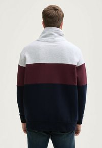 Maglione con colletto alto, caratterizzato da righe orizzontali grigie, bordeaux e blu navy. Realizzato in tessuto morbido con polsini e orlo a costine.