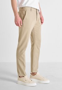 Pantalones de algodón beige con un corte recto y bolsillos laterales, combinados con zapatillas beige claro que tienen una suela texturizada y cordones.