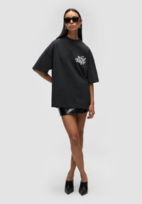 T-shirt noir oversize en tissu doux avec un texte graphique blanc. Associé à une mini jupe noire brillante et des chaussures à talons noirs pointus.