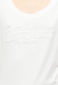 Λευκό βαμβακερό t-shirt με λαιμόκοψη scoop, που διαθέτει ανάγλυφο υφασμάτινο λογότυπο "Guess" και τη φράση "est. 1981" σε διακριτικό γκρι χρώμα.