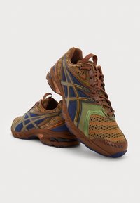 Bruna och gröna nätaktiga träningsskor med blåa detaljer, texturerad yta och mönstrade överlägg. Har en hållbar gummisula och snörningsdesign.
