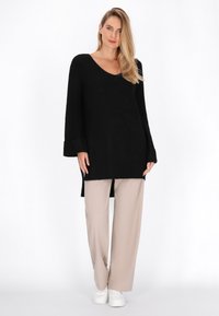Pulover negru tricotat cu decolteu în V și mâneci lungi, asociat cu pantaloni bej cu picioare largi și adidași albi, având deschideri laterale.
