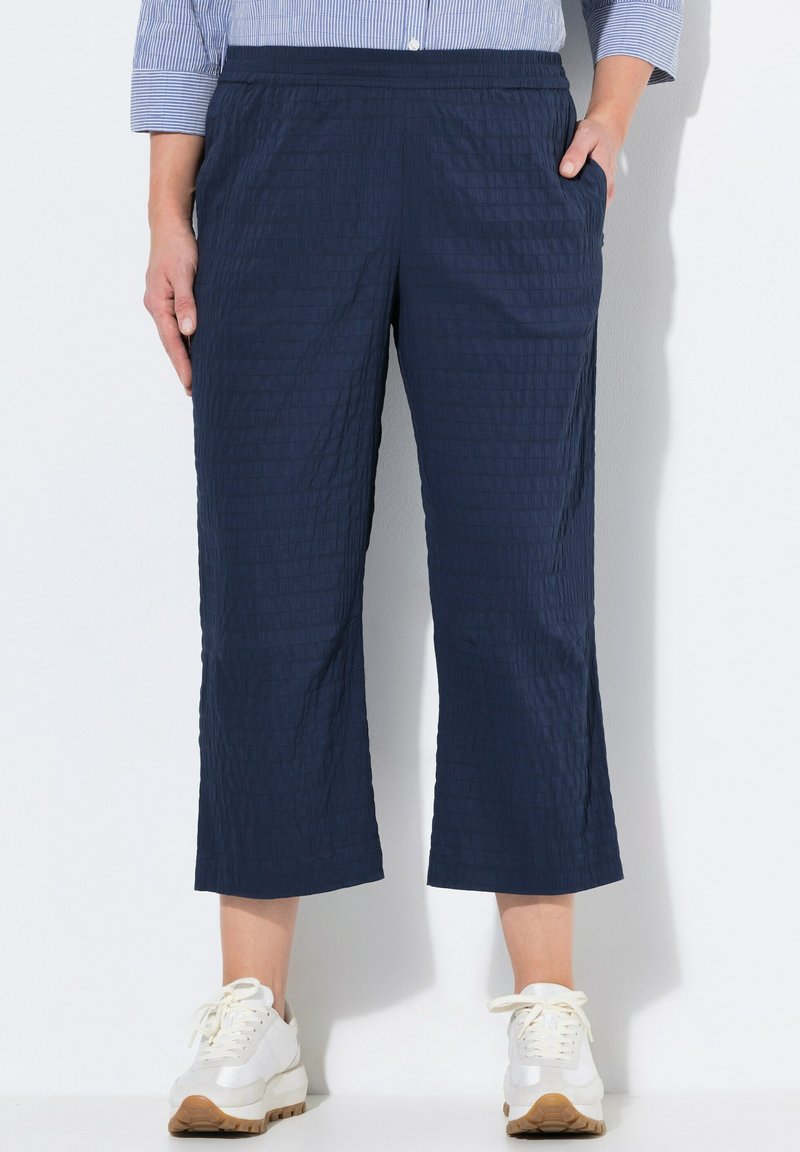 Navyblauwe cropped broek van een gestructureerde stof, met een elastische tailleband en zijzakken, gecombineerd met witte sneakers.
