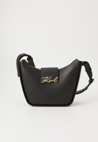 Svart lærveske med gullhardware, som har glidelås og en frontklaff med navnet "Karl" preget i kursiv.