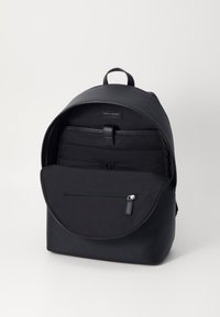 Mochila de cuero negra con textura suave, parte superior redondeada, cierre de solapa frontal y compartimentos interiores, incluyendo un bolsillo con cremallera.