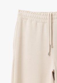 Helle beigen Sweatpants aus weichem Stoff, mit einem elastischen Bund und Kordelzug, Seitentaschen und einer glatten Textur.