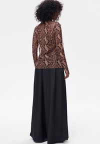 Top z długim rękawem w wężowy wzór o dopasowanym kroju, zestawiony z wysokim stanem i szerokimi nogawkami czarnych spodni wykonanych z gładkiej tkaniny.