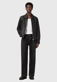Schwarze Lederjacke mit Reißverschluss, weißes geripptes Shirt und schwarze Jeans mit geradem Schnitt. Schwarze Schuhe mit sichtbaren Nähdetails.