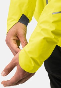 Neongelb fluoreszierende Regenjacke mit elastischen Bündchen und grauem Innenfutter, showcasing Hände, die den Ärmel für eine optimale Passform und Komfort anpassen.