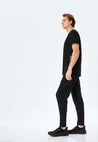 Camiseta negra con cuello redondo, combinada con pantalones negros ajustados y zapatillas deportivas negras con una parte superior texturizada y suela de goma.