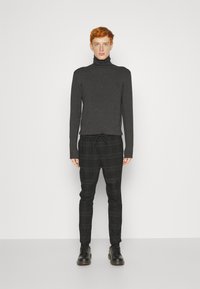 Suéter de cuello alto gris oscuro combinado con pantalones a cuadros negros y grises, con cintura ajustable, corte slim y zapatos negros de cordones.