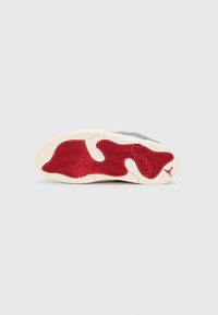 Sola di sneaker in bianco sporco con un motivo in gomma rossa ondulata. È visibile un logo. Il colore predominante è grigio con dettagli testurizzati.