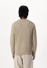 Beżowy sweter z prążkowanego dzianiny z długimi rękawami, okrągłym dekoltem i dopasowanymi mankietami, pokazany od tyłu na białym tle.