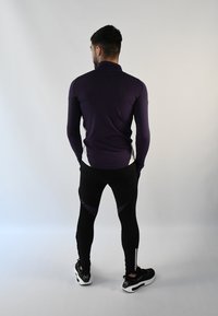 Top de manga larga púrpura con cuello alto, combinado con leggings negros con detalles púrpuras y cremalleras en los tobillos, llevados con zapatillas negras.