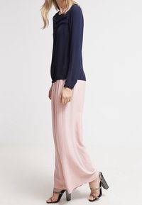 Blusa navy a maniche lunghe con dettaglio arricciato sul colletto abbinata a pantaloni a gamba larga rosa chiaro e sandali neri con tacco.