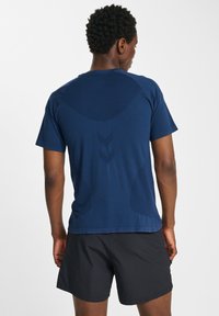 Marinblå atletisk t-shirt med korta ärmar, som har en slät textur och diskreta logodetaljer på baksidan, i kombination med svarta shorts.