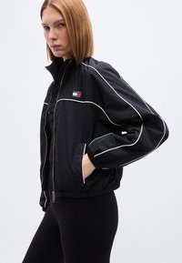 Μαύρο μπουφάν τύπου bomber από νάιλον με λευκή διακόσμηση, κλείσιμο με φερμουάρ και πλαϊνές τσέπες. Διαθέτει πολύχρωμο λογότυπο στο στήθος.