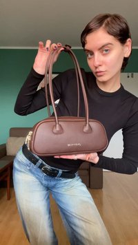 Mala de mão em couro castanho com duas alças, forma oval e fecho de correr. Apresenta um relevo subtil com a palavra "VALENTINO" na parte da frente.