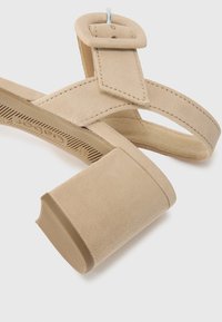 Beige nubukist kõrged sussid, millel on lai plokknina, kaks õhukest rihma ja suur ümmargune nööbikas. Reljeefne tall, et tagada haardumine.