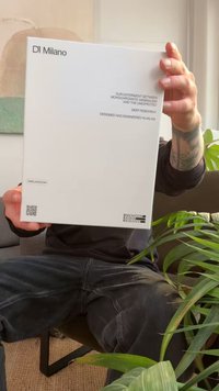 Witte rechthoekige doos met "DI Milano" branding, tekst aan de voorkant, QR-codes en hashtags. Omringd door groen op een zachte ondergrond.