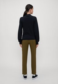 Zwarte trui met lange mouwen, gecombineerd met smalle olijfgroene broek en zwarte sneakers. Soepele textuur, casual ontwerp.