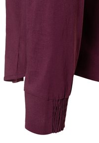 Burgunderfarbene Bluse mit weicher Textur, ausgestattet mit einem gerafften Ärmel-Design und leichten seitlichen Schlitzdetails für zusätzlichen Komfort.