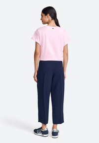 Roze cropped t-shirt met opgerolde mouwen, gecombineerd met marineblauwe wijde broekspijpen. De outfit heeft een klein logo op de achterkant en comfortabele sneakers.