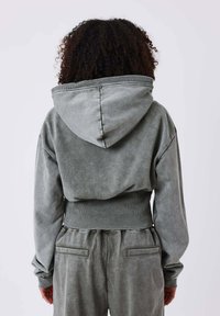 Grijze cropped hoodie van zacht materiaal, met een grote capuchon, geribbelde manchetten en een comfortabele pasvorm. Opvallende vervaagde textuur en stikseldetails.
